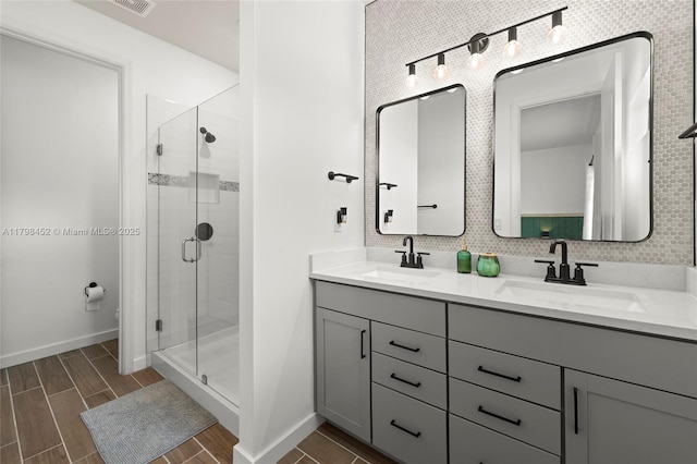 bathroom with a shower stall, double vanity, baseboards, and wood finished floors