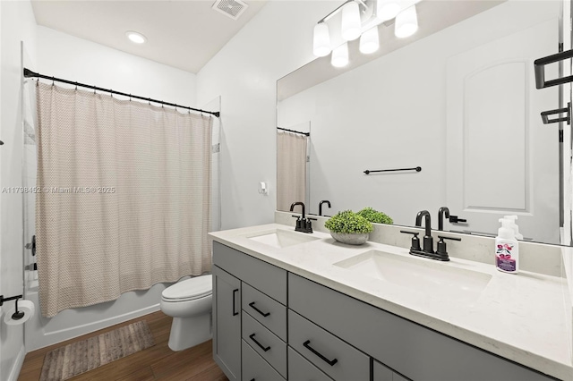 bathroom featuring toilet, wood finished floors, double vanity, and shower / tub combo