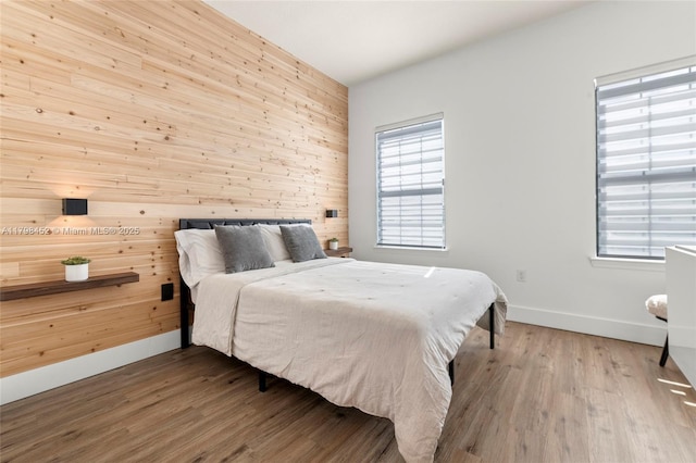 bedroom featuring baseboards, wooden walls, and wood finished floors