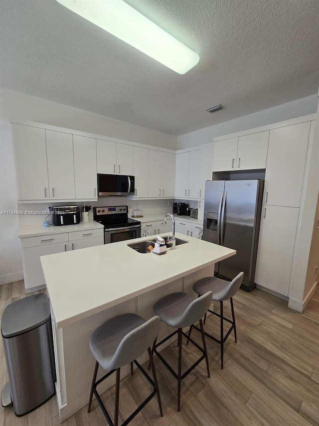 17545 SW 150th Ct, Miami, FL 33187 - kitchen with stainless steel appliances, a sink, a kitchen bar, light wood-style floors, and a textured ceiling
