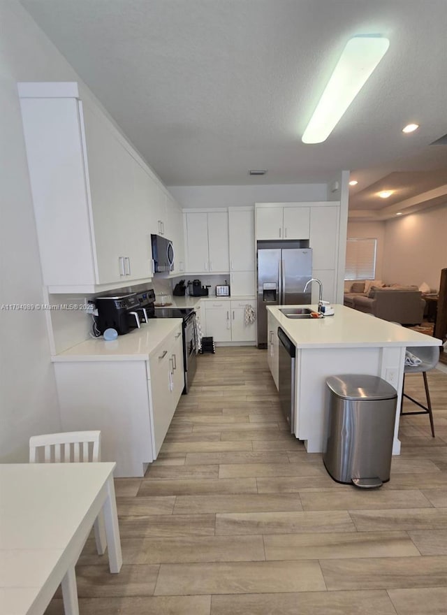 17545 SW 150th Ct, Miami, FL 33187 - kitchen featuring appliances with stainless steel finishes, light wood finished floors, a sink, a center island with sink, and white cabinetry