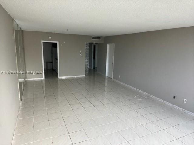 spare room with a textured ceiling, light tile patterned floors, and baseboards