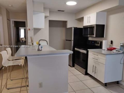 kitchen with stainless steel appliances, white cabinetry, a breakfast bar area, and light tile patterned floors
