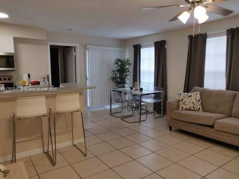 living room featuring a ceiling fan, light tile patterned floors, and baseboards