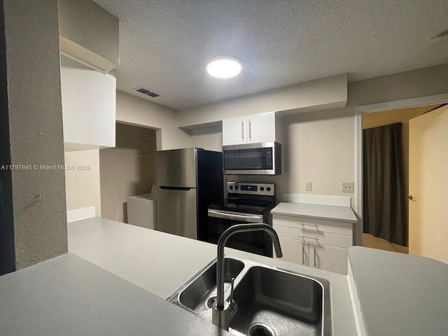 kitchen featuring stainless steel appliances, a sink, light countertops, white cabinets, and a textured ceiling