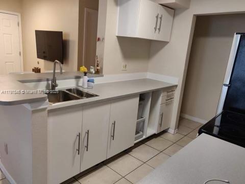 kitchen with freestanding refrigerator, white cabinetry, light tile patterned floors, light countertops, and a sink