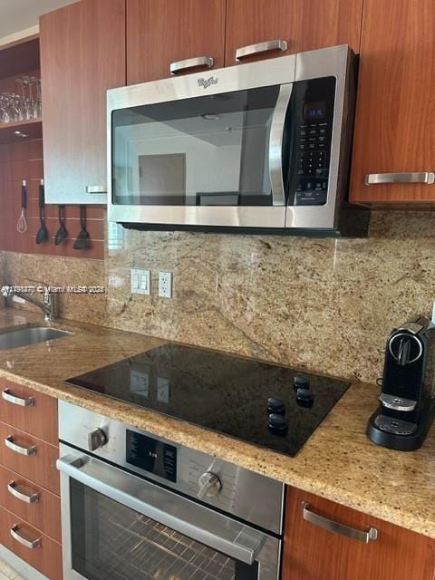 kitchen featuring appliances with stainless steel finishes, a sink, backsplash, and brown cabinets