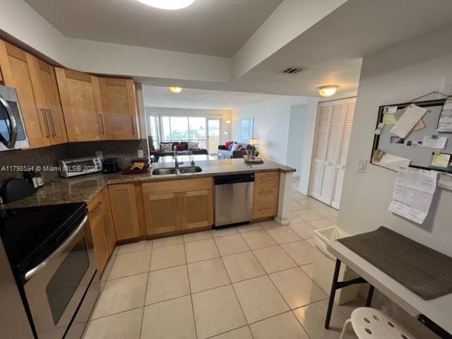 kitchen with stainless steel appliances, a sink, a peninsula, backsplash, and light tile patterned floors