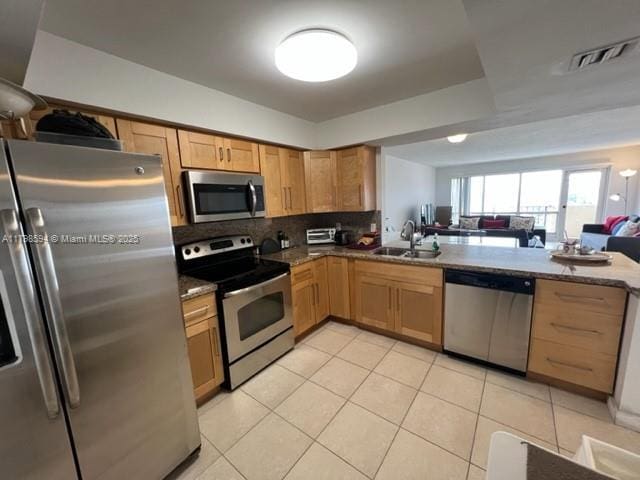 kitchen with appliances with stainless steel finishes, a sink, light tile patterned floors, open floor plan, and backsplash
