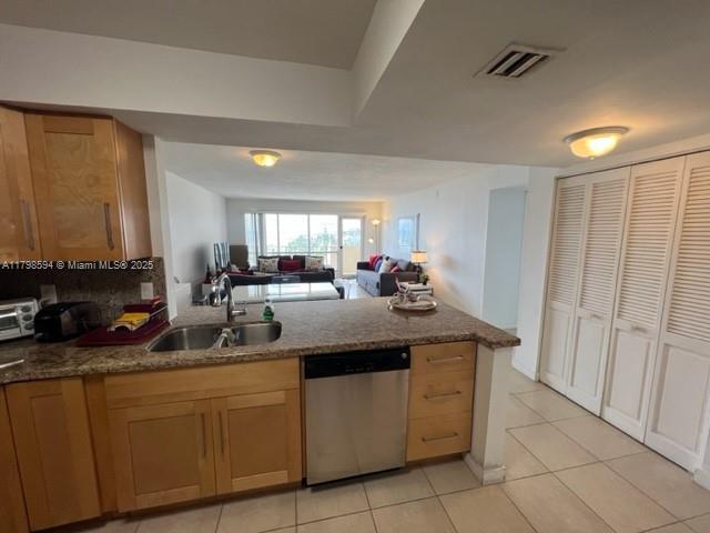 kitchen featuring dishwasher, a sink, light tile patterned flooring, open floor plan, and a peninsula