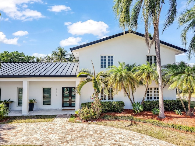 rear view of house with stucco siding, a standing seam roof, french doors, and metal roof