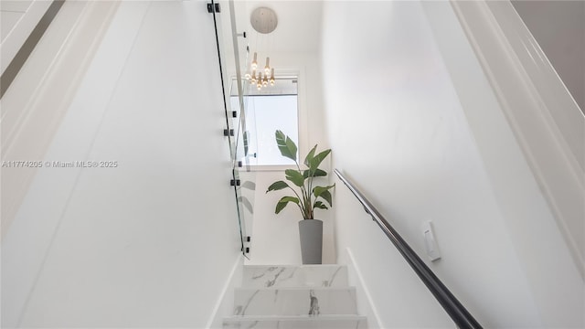 staircase with marble finish flooring, a chandelier, and baseboards