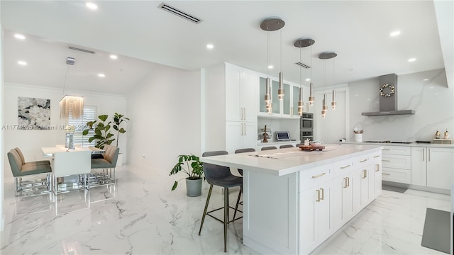 kitchen with wall chimney range hood, light marble finish floors, glass insert cabinets, a kitchen island, and white cabinetry