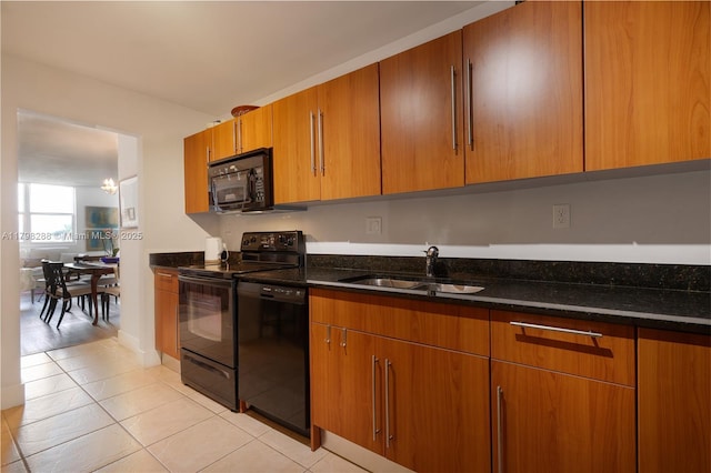 kitchen with black appliances, a sink, light tile patterned flooring, dark stone countertops, and brown cabinetry