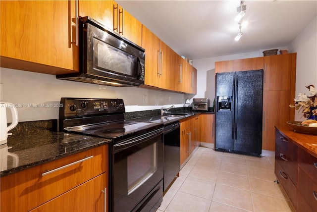 kitchen with black appliances, light tile patterned floors, dark stone counters, and brown cabinetry