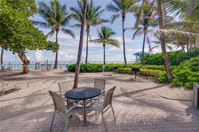 view of community with fence, a water view, outdoor dining space, and a patio