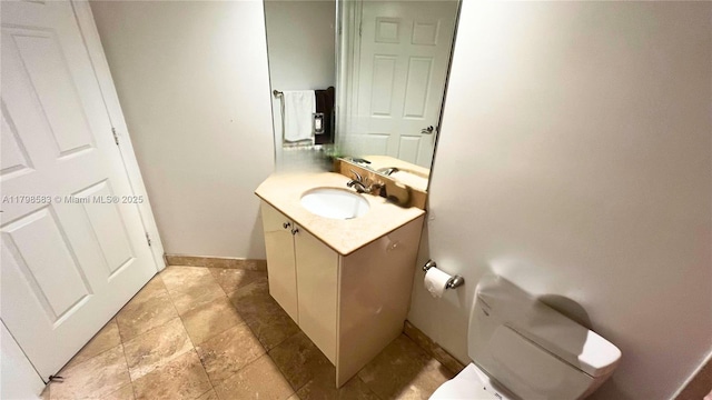 bathroom featuring baseboards, stone tile flooring, vanity, and toilet