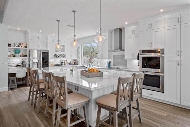 1199 NW 166th Ave, Pembroke Pines, FL 33028 - kitchen featuring stainless steel appliances, wall chimney exhaust hood, white cabinets, backsplash, and light wood-style floors