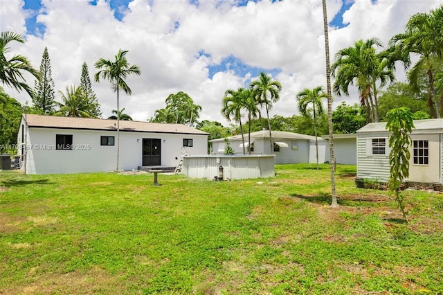 rear view of house featuring a swimming pool, a lawn, and an outbuilding