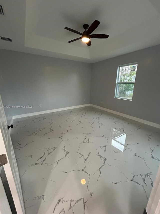 empty room with a raised ceiling, ceiling fan, baseboards, and marble finish floors