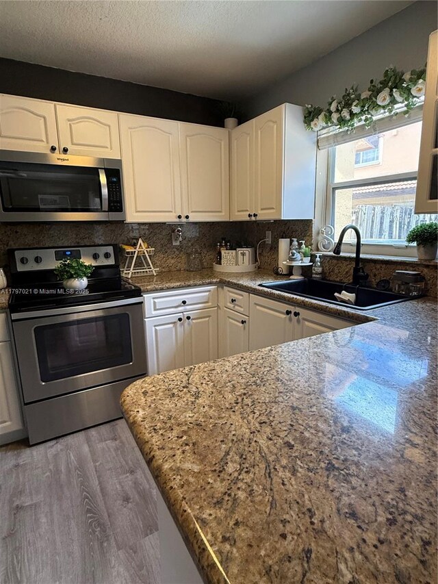 238 Magnolia Ave, Davie, FL 33325 - kitchen with stainless steel appliances, a sink, white cabinetry, wood finished floors, and dark stone counters