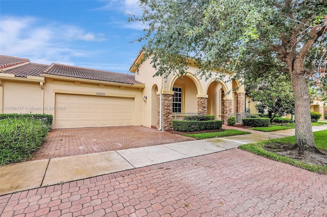 mediterranean / spanish-style home featuring stucco siding, decorative driveway, a garage, and a tile roof