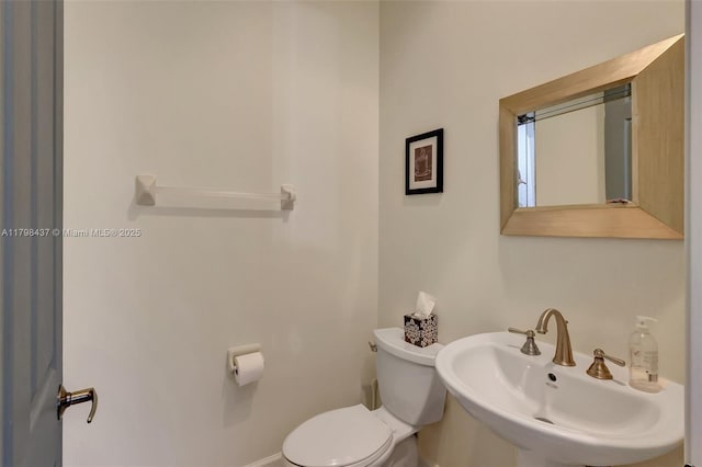 half bathroom with a sink, toilet, and baseboards