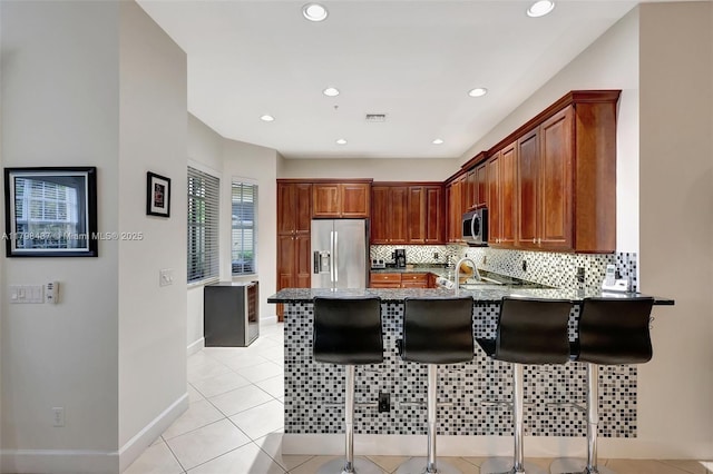kitchen with stainless steel appliances, a peninsula, tasteful backsplash, a breakfast bar area, and light stone counters