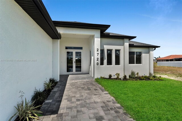 1212 NW 35th Pl, Cape Coral, FL 33993 - view of exterior entry with french doors, stucco siding, and a yard