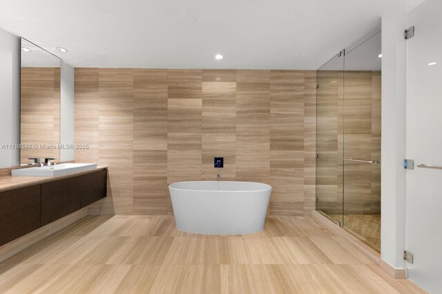 bathroom with tile walls, a freestanding bath, a stall shower, vanity, and recessed lighting
