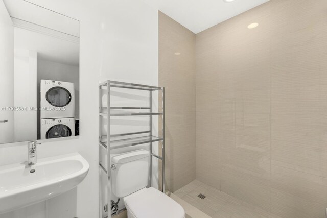 bathroom featuring stacked washer / drying machine, a sink, toilet, and a tile shower