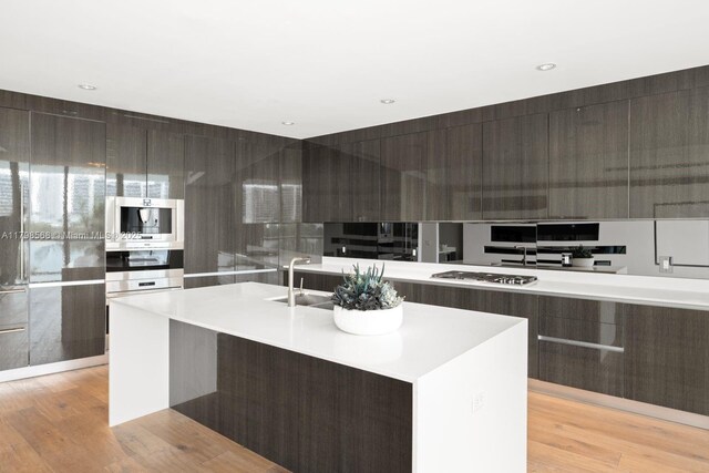 kitchen featuring modern cabinets, a sink, an island with sink, light countertops, and light wood finished floors