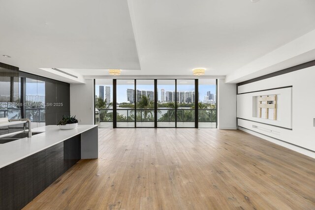 unfurnished living room featuring a wall of windows, a sink, a city view, and light wood-style floors