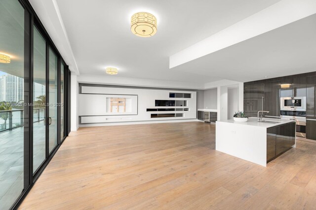 kitchen featuring modern cabinets, light wood finished floors, light countertops, a sink, and a center island with sink
