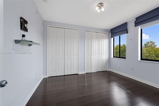 unfurnished bedroom featuring multiple closets, baseboards, and wood finished floors