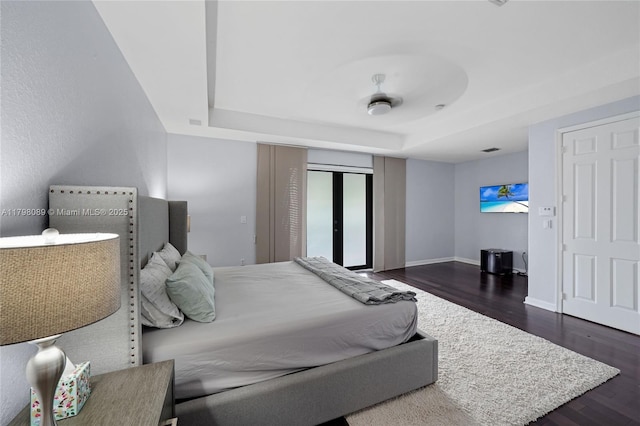 bedroom with a raised ceiling, dark wood-style flooring, a closet, and baseboards
