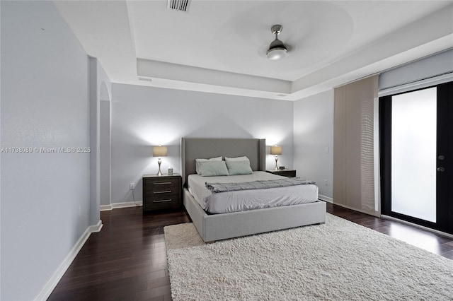 bedroom featuring wood finished floors, a tray ceiling, baseboards, and access to exterior