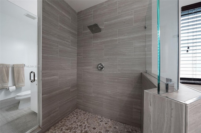 bathroom with tiled shower, toilet, and healthy amount of natural light