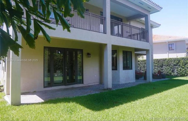 rear view of property featuring stucco siding, a lawn, and a balcony