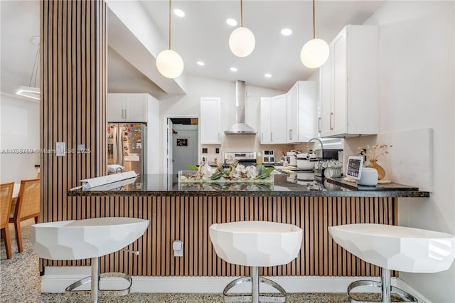 kitchen featuring stainless steel fridge, wall chimney exhaust hood, a peninsula, hanging light fixtures, and white cabinets