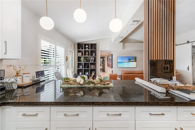 kitchen featuring open floor plan, vaulted ceiling, white cabinetry, dark stone countertops, and decorative light fixtures