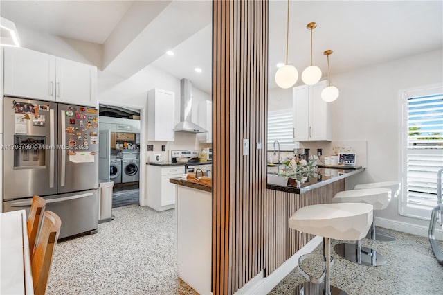 kitchen featuring stainless steel appliances, wall chimney exhaust hood, washing machine and dryer, a sink, and dark countertops