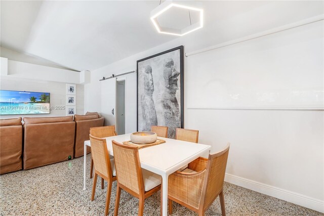 dining room featuring dark speckled floor, lofted ceiling, baseboards, and a barn door