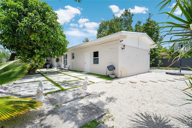 rear view of property featuring a patio area, fence, and stucco siding