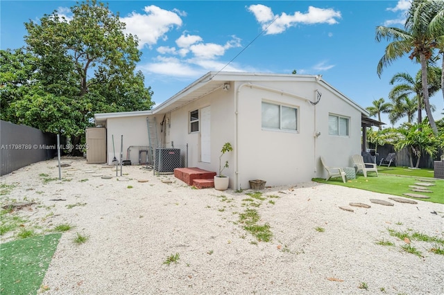 rear view of property with fence, stucco siding, and central AC