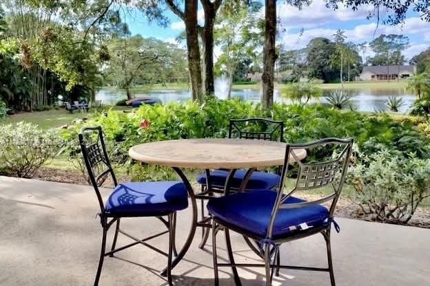 view of patio / terrace featuring a water view, outdoor dining area, and view of wooded area