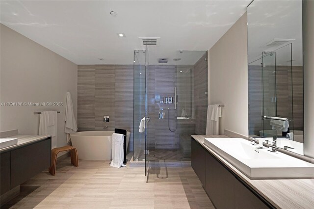 bathroom featuring a stall shower, vanity, a freestanding bath, and tile walls