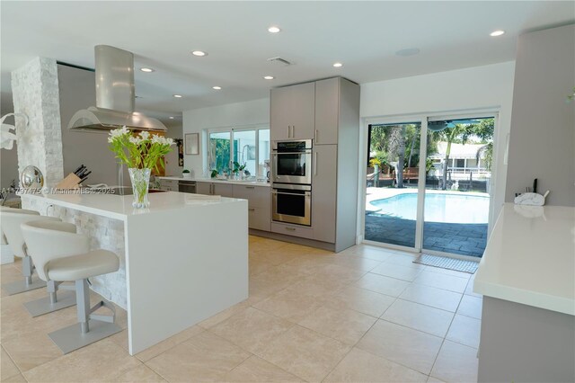 2711 NE 57th Ct, Fort Lauderdale, FL 33308 - kitchen with island range hood, appliances with stainless steel finishes, light countertops, a kitchen breakfast bar, and plenty of natural light