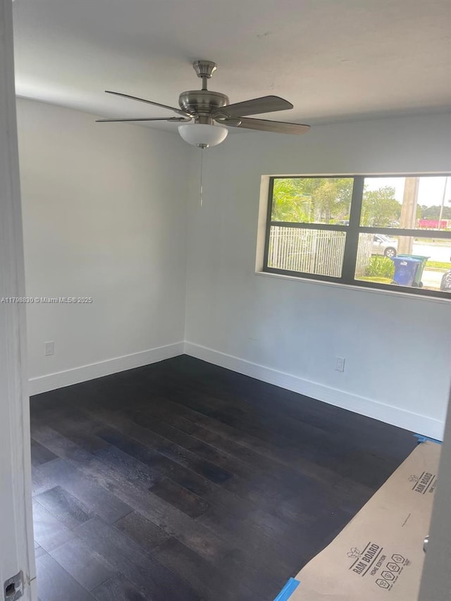 spare room with dark wood-type flooring, a ceiling fan, and baseboards