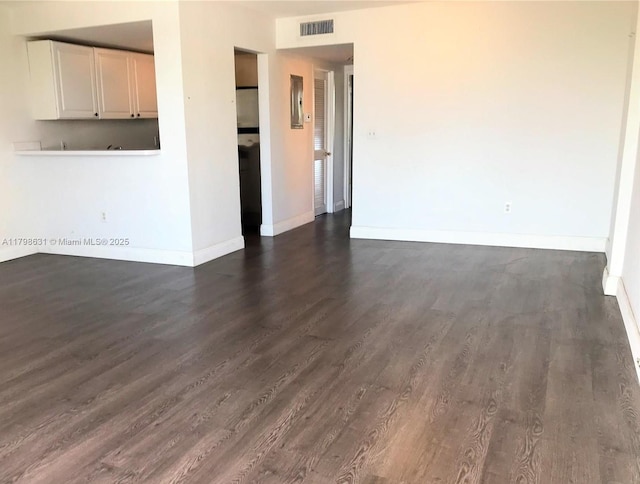 unfurnished living room featuring baseboards and dark wood-type flooring